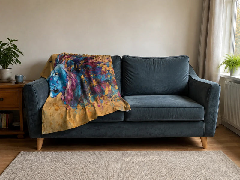 Lion's Sunset Blanket draped over the left side of a blue-grey sofa, viewed straight-on in a living room with plants, a side table and a rug.
